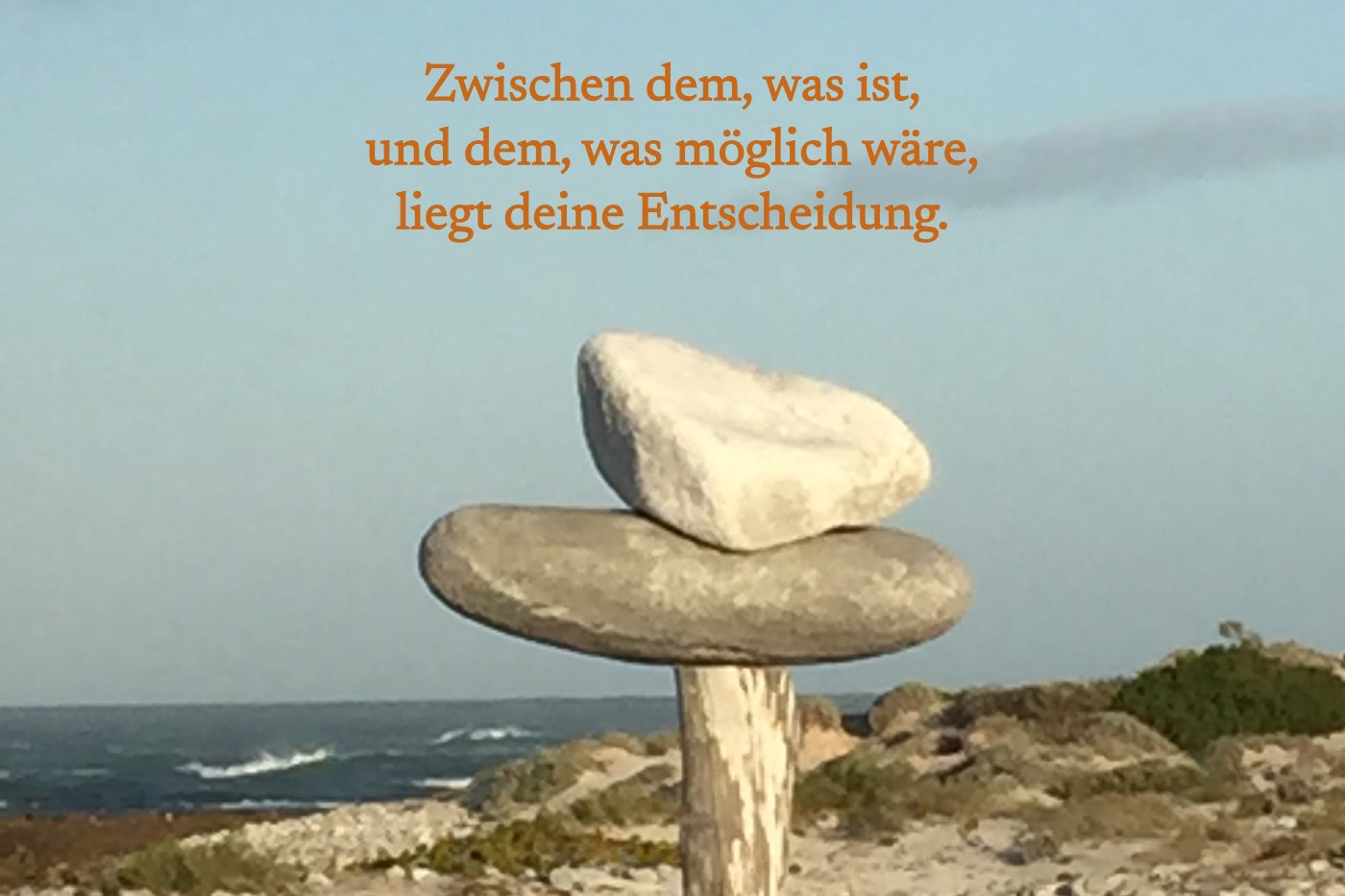 Zwei Steine liegen aufeinander auf einem Holzpfahl am Meer, mit dem Satz: Zwischen dem, was ist, und dem, was möglich wäre, liegt deine Entscheidung.