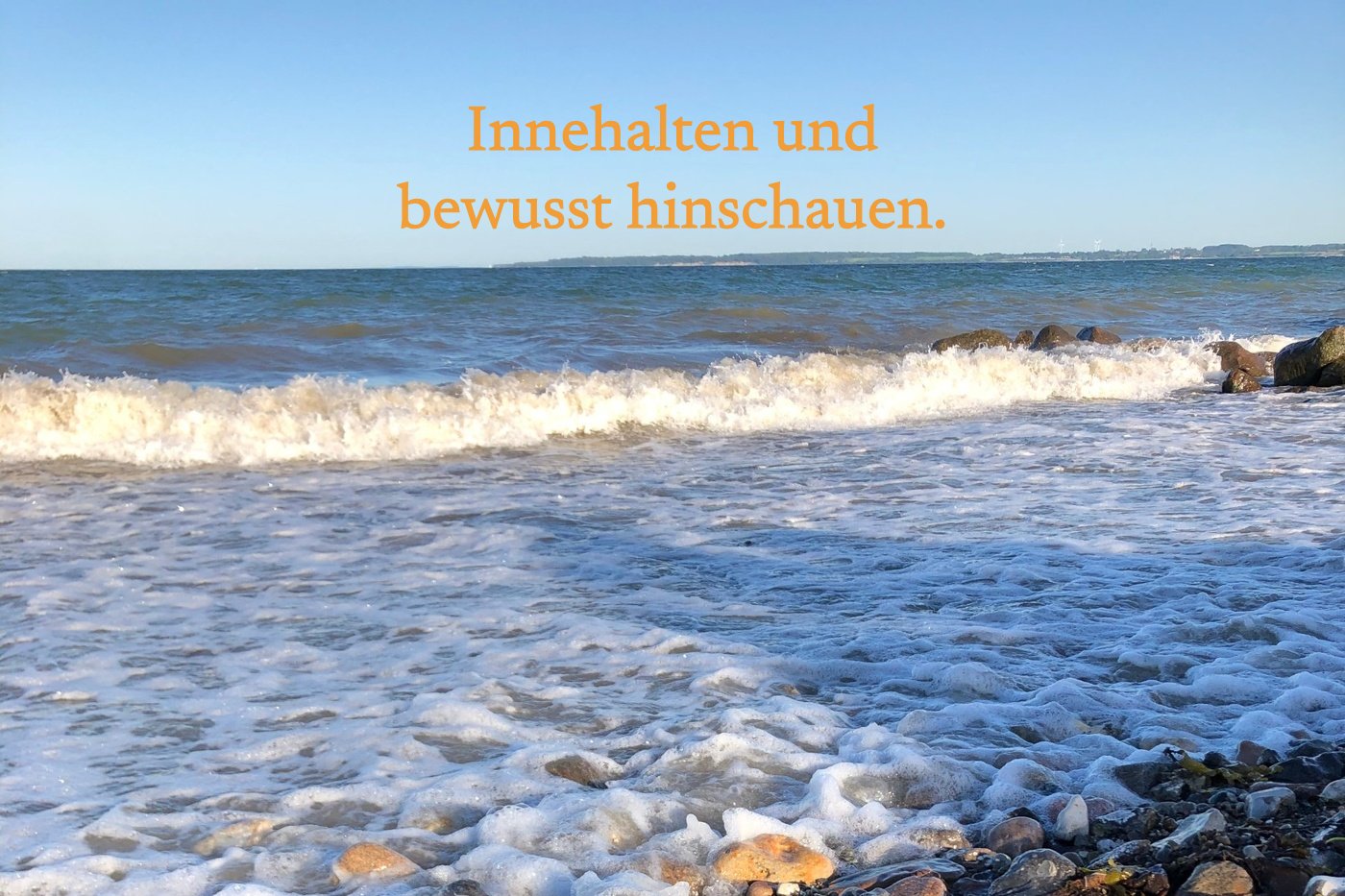 Wellen laufen auf einen Steinstrand, mit dem Satz: Innehalten und bewusst hinschauen.